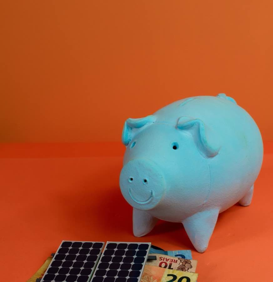 Cofrinho ao lado de um painel solar em miniatura e notas de real
